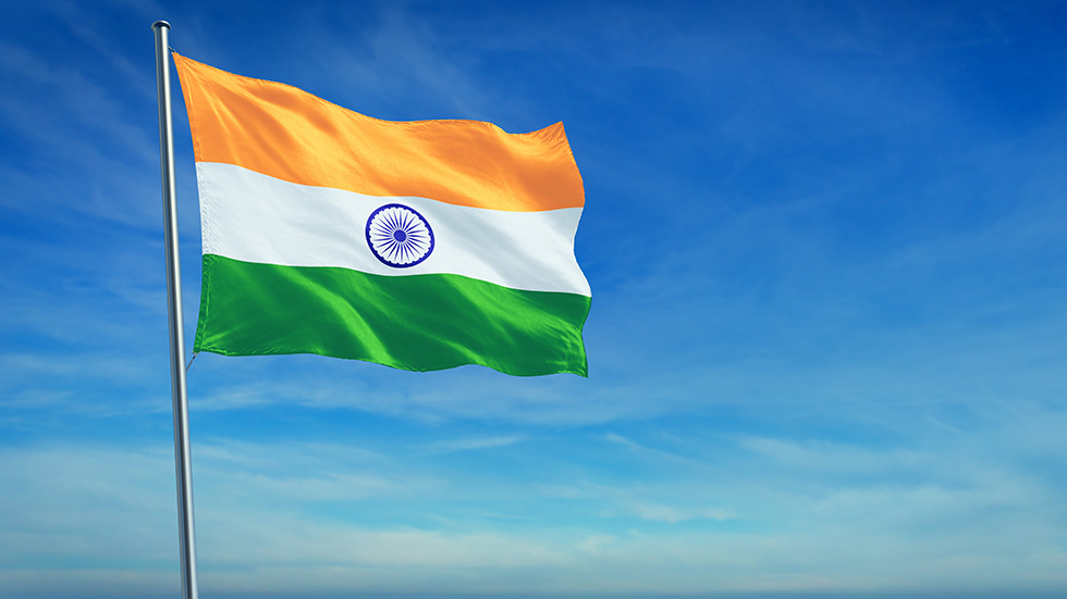 The National flag of India blowing in the wind in front of a clear blue sky